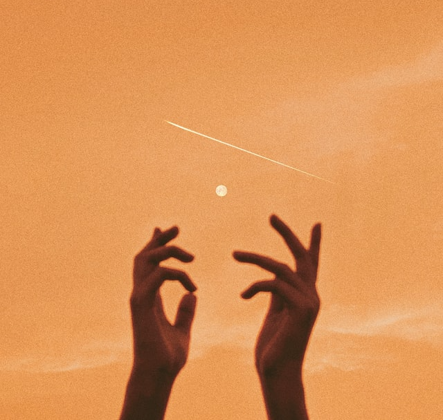 Close-up of hands reaching into the air in front of an orange sky.