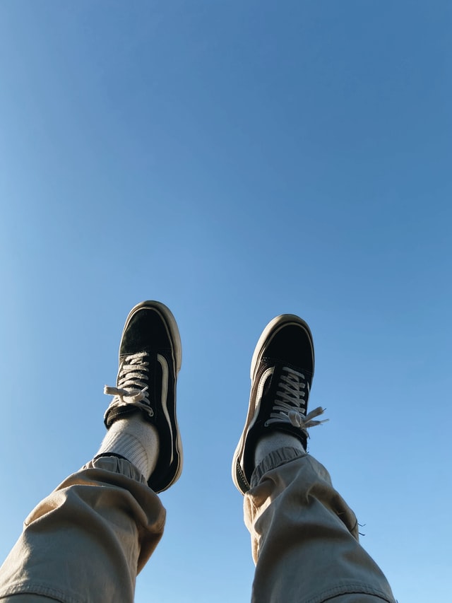Feet with shoes stretching into the air in front of a wide blue sky