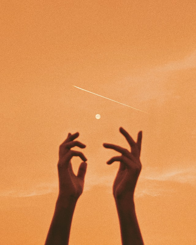 Close-up of hands reaching into the air in front of an orange sky.